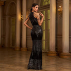 Woman in a black sequin evening gown standing in an elegant interior setting.