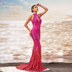 Woman in a pink evening gown standing on a beach with ocean waves in the background