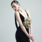 Woman wearing a black dress with a large green flower accessory on a plain background