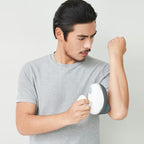 Man using a white and gray massage device on his arm against a light gray background