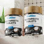 Two bottles of OralGos toothpaste tablets on a bathroom counter with text about cleansing.