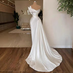 White off-shoulder evening gown on a mannequin in a room with a couch and plant.