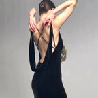 Woman wearing a black dress with a deep neckline and thin straps against a gray background