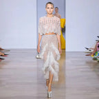 Model walking on a runway wearing a stylish outfit with a top and skirt.