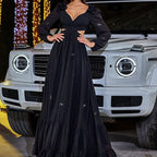 Woman in a black dress standing in front of a silver SUV with festive lights in the background