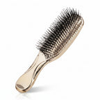 Gold hairbrush with black bristles next to its packaging on a white background