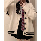 A person wearing an oversized cream knit cardigan with black trim, a white top, a red striped tie, and a black pleated skirt, photographed indoors in a mirror selfie.