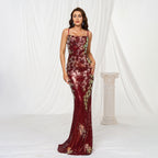 Woman wearing a burgundy evening gown with floral embroidery against a white curtain background