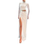 Woman wearing a white evening gown with a high slit in front of a Christmas tree and decorated wall.