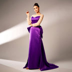 Woman in a long purple evening gown with beige sleeves against a neutral background