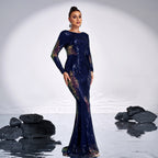 Woman in a dark blue sequin gown standing in water with rocks on a white background
