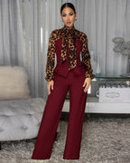 Woman wearing a leopard print top and burgundy pants in a stylish room.