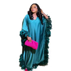 Woman in a teal dress with green trim holding a pink clutch against a beige curtain background