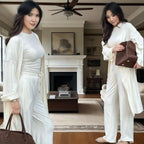 Woman in a white outfit holding a brown bag in a living room.