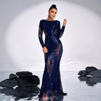 Woman in a blue evening gown standing on a reflective surface with black rocks and a white background