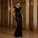 Woman in a black sequin evening gown standing in an elegant interior setting.