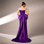 Woman wearing a purple evening gown with a large bow on a neutral background