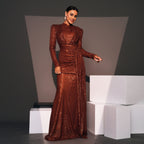 Woman in a brown sequined gown standing on white blocks against a dark background