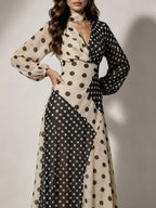A woman modeling a long-sleeve maxi dress with a beige and black polka dot patchwork design, featuring a high neck and wrap-style bodice.