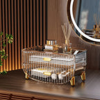 Clear decorative organizer with gold accents on a wooden surface, featuring Chanel products.