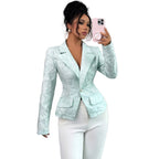 A woman takes a mirror selfie wearing a fitted, long-sleeve light mint green jacquard blazer with white trousers. She holds a pink smartphone with a pop socket.