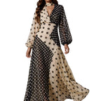 A woman models a long-sleeved maxi dress with a beige and black polka dot pattern, featuring a high neck, keyhole cutout at the chest, and balloon sleeves, set against a neutral studio background with dramatic lighting.