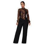 A woman models a high-neck long-sleeve blouse with a leopard print and black corset-style bodice, paired with black wide-leg trousers, in a modern living room setting.