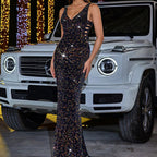 Woman in a sparkling evening gown standing in front of a white luxury SUV with festive lights in the background.