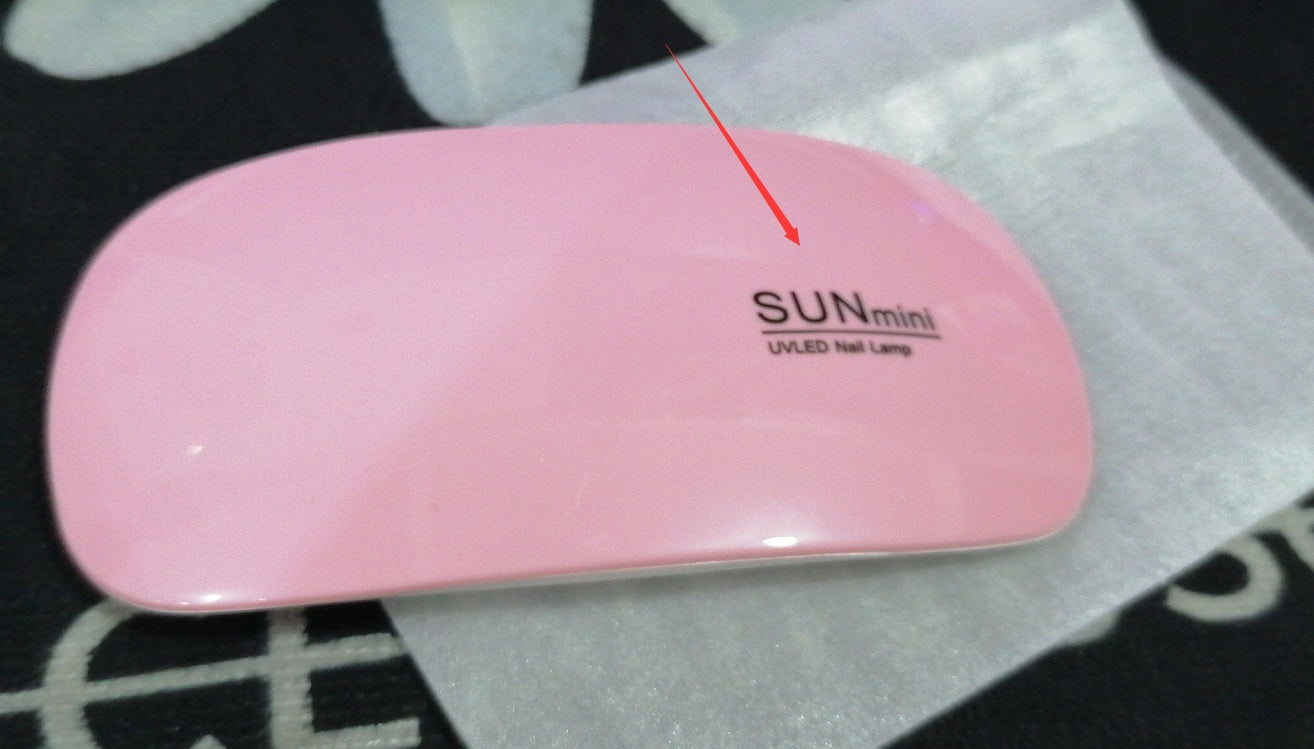 Pink UV/LED nail lamp with 'SUN mini' branding on a black and white patterned surface.