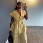 Woman in a yellow outfit taking a mirror selfie in a room with wooden flooring.