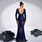 Woman in a blue evening gown with a low back, standing in a reflective surface with black rocks.