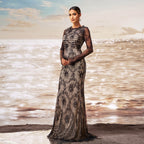 Woman in a black and silver evening gown standing on a beach with ocean waves in the background