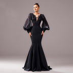 Woman wearing a black evening gown with sheer sleeves against a gray background