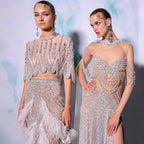 Two models wearing sparkling, beaded outfits against a light background