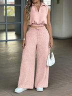 Woman wearing a pink outfit with geometric patterned pants and matching top, holding a white handbag.
