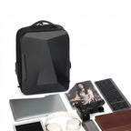 A black geometric laptop backpack displayed on a white background with various tech accessories and a photo print arranged around it.