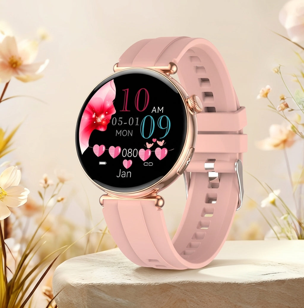 A smartwatch with a round black display and a light pink silicone strap, shown standing on a stone surface with soft floral background blur.