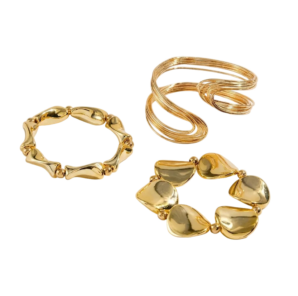 Three gold-toned jewelry pieces arranged on a clean white background: a wide textured ring bracelet, a chunky coiled ring, and a heart-link bracelet.