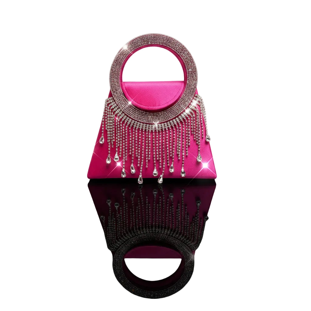 A bright pink velvet evening clutch bag with a circular top handle, heavily embellished with silver rhinestones and dangling crystal chains, set against a plain white background.