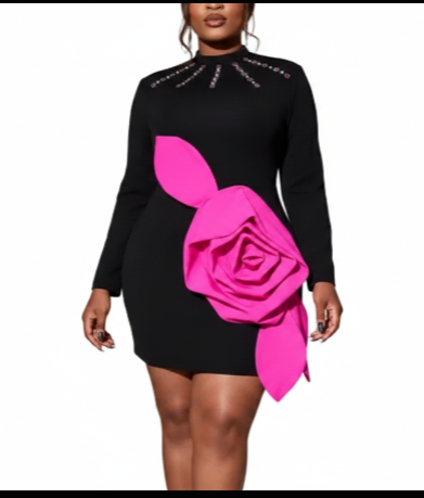 A woman modeling a black long-sleeve mini dress with a large hot pink fabric rose applique on the front and rhinestone embellishments around the neckline, set against a plain white background.