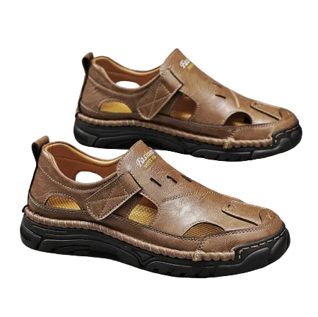 A pair of men's brown leather slide sandals with hook-and-loop straps and thick black soles, displayed on a gray surface with one shoe resting on a white box.