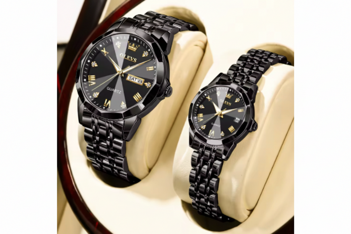 Two black metal wristwatches with black link bands and gold-tone details, displayed on cream-colored cushioned stands. One watch face is shown in full and the other is cropped, with a red OLEVS logo overlay in the top-left corner.