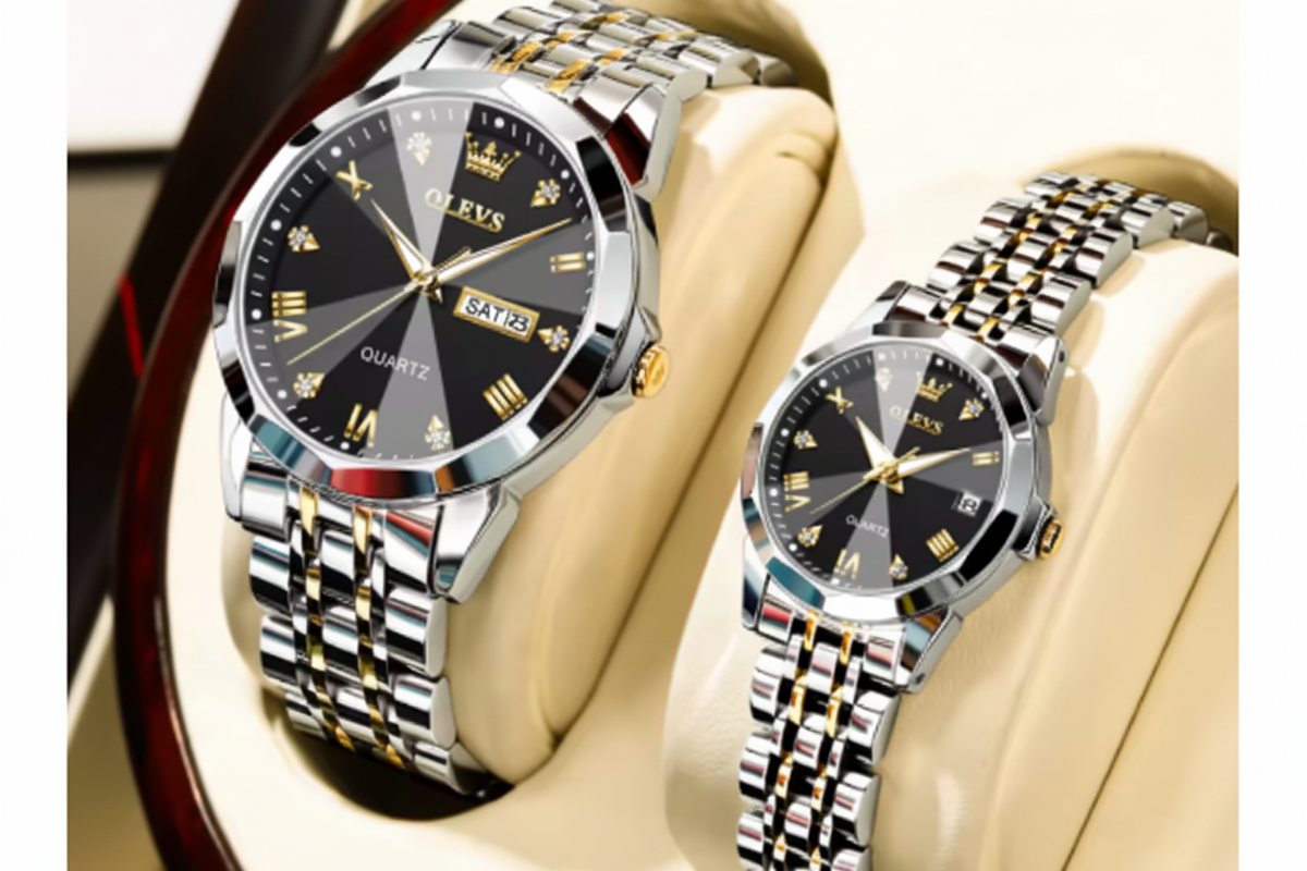 Two OLEVS men's analog watches displayed on cream-colored watch stands. The watches feature polished silver-tone stainless steel cases and multi-link metal bracelets with gold-tone accents, black dials with gold Roman numerals, and date windows.