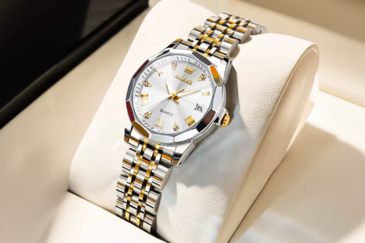 Olevs men's analog watch with a silver and gold-tone stainless steel link bracelet, a white dial with gold details, and a date window, displayed on a cream-colored watch cushion.