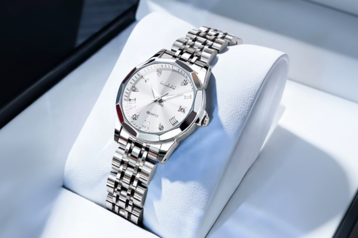 A silver stainless steel wristwatch with a white dial and crystal glass, resting on a white display cushion. The brand name 'OLEVS' is visible in a red logo overlay in the top-left corner.