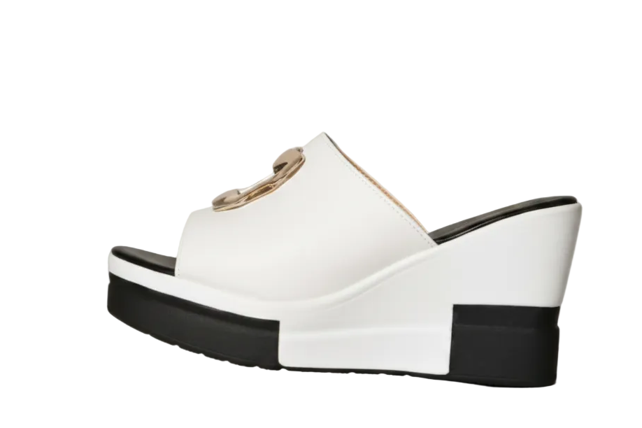 White platform wedge sandals with cutout straps and black soles, shown on a model's feet in a minimalist indoor setting.