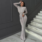 Woman in a silver evening gown standing on a staircase with dark walls and marble steps.