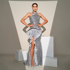 Woman in a silver evening gown standing on a white platform with a neutral background