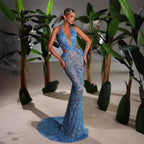 Woman in a blue sparkly evening gown standing among plants.