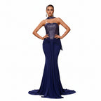 Woman in a blue evening gown standing in an elegant interior setting with stairs and classical sculpture.
